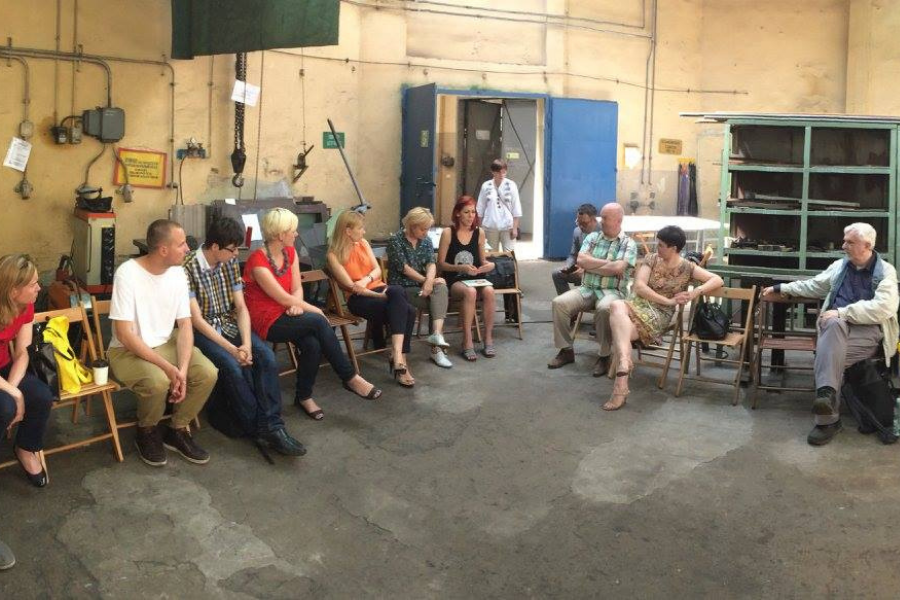 Zdjęcie przedstawia grupę osób - kobiet i mężczyzn - siedzących na krzesłach w zamkniętym pomieszczeniu typu warsztat. Osoby dyskutują podczas szkolenia.