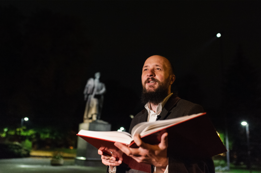 Noc. Mężczyzna trzyma otwartą książkę. W tle rozmazany pomnik Adama Mickiewicza w Gliwicach.