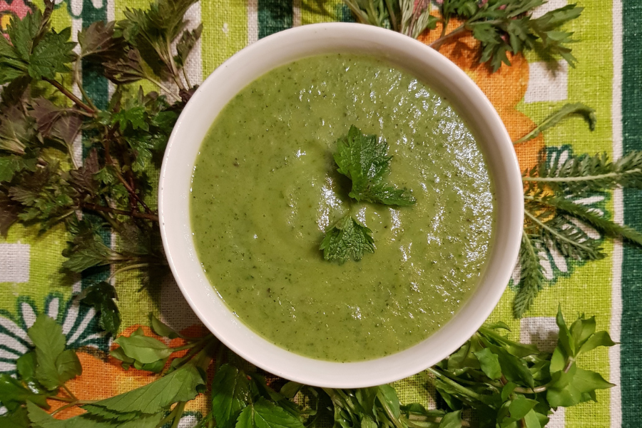 Zielona zupa krem z cukinii z ziolami wyserwowana w talerzu. Pod talerzem obrus z motywami roślinnymi
