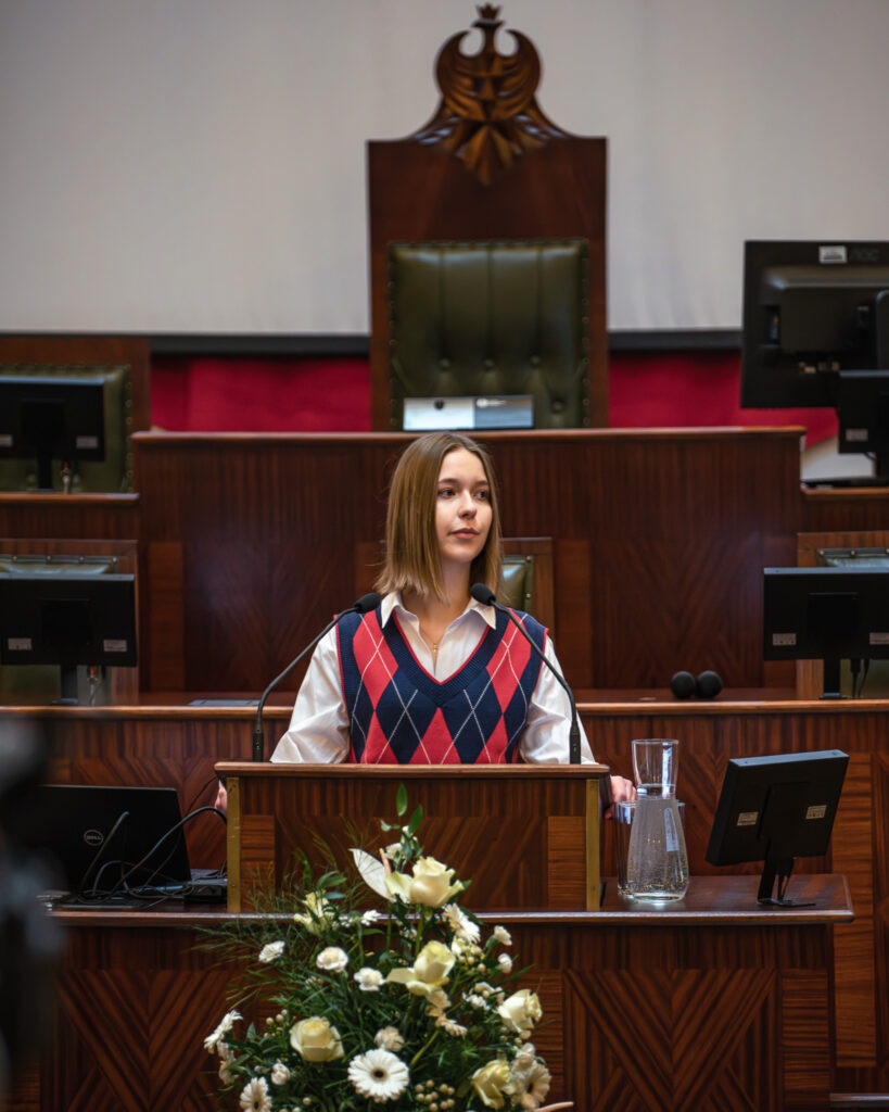 Młoda dziewczyna przemawia w sali Sejmu Śląskiego podczas konkursu