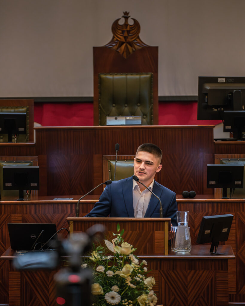 Młody chłopak przemawia w sali Sejmu Śląskiego podczas konkursu