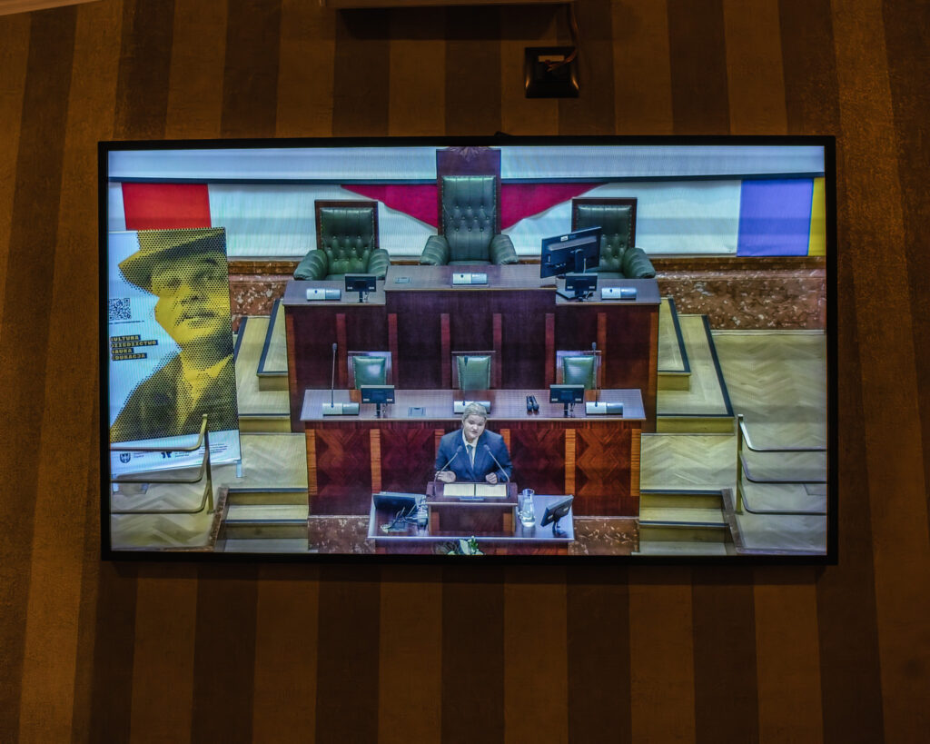 Ekran telewizora przedstawia młodą dziewczynę przemawiającą w sali Sejmu Śląskiego podczas konkursu