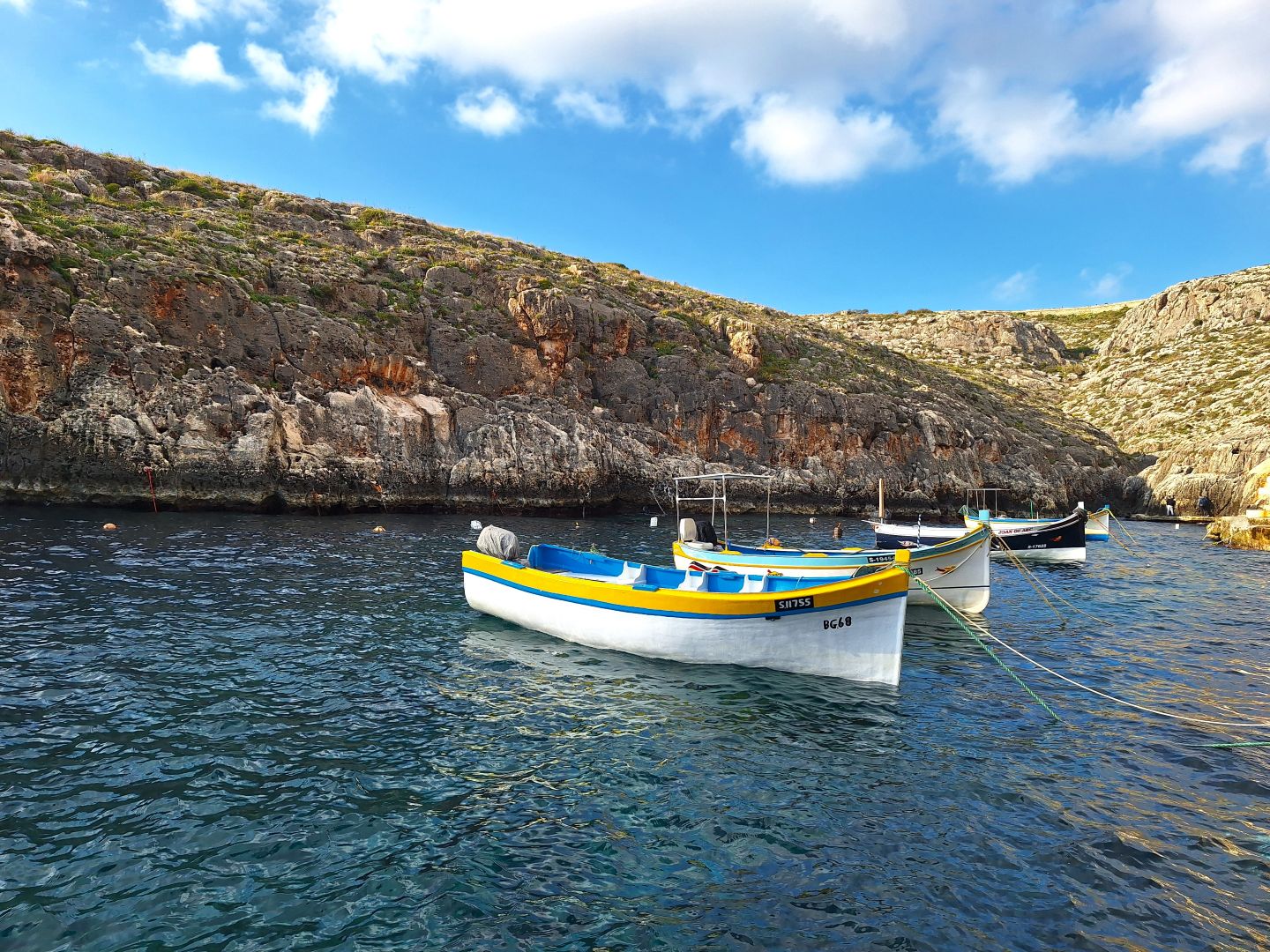 Trzy biało-żółte łódki przycumowane do wybrżeża Blue Gotto na Malcie